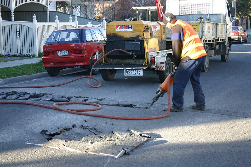 Operador utiliza um martelo pneumático ligado por mangueira a um compressor.