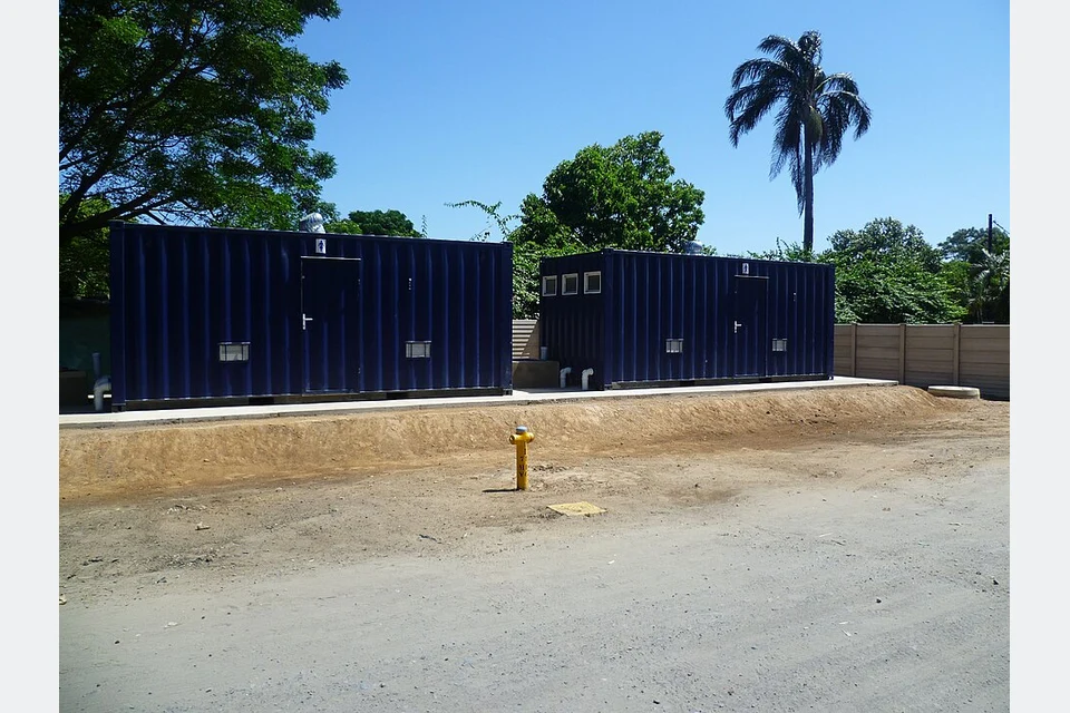 Exterior de módulos sanitários em contentores, com portas e tubagens.
